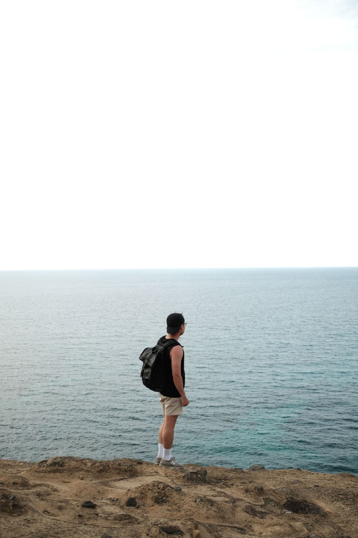 A man with a backpack looking out to sea from the edge of a cliff