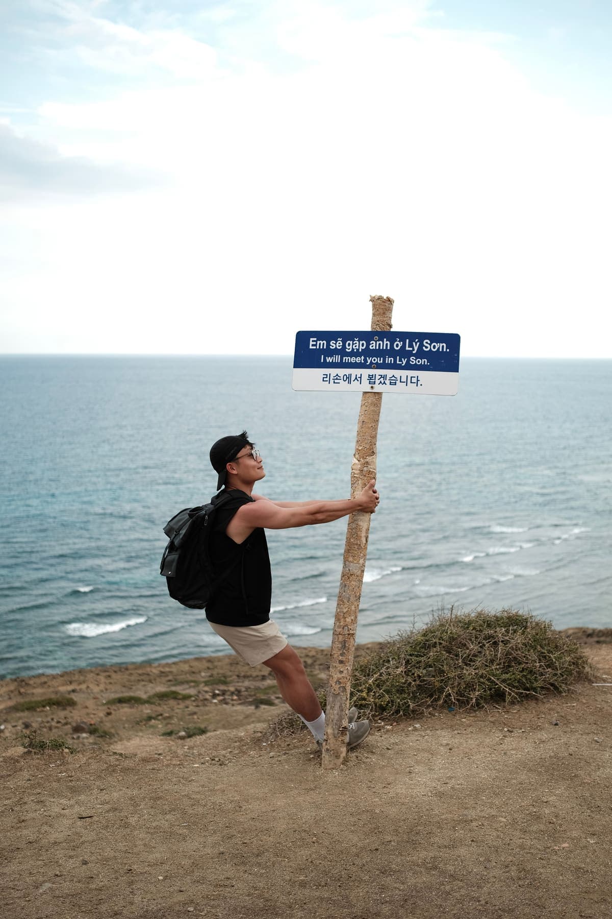 A man leaning back against a signpost reading “I will meet you in Ly Son”