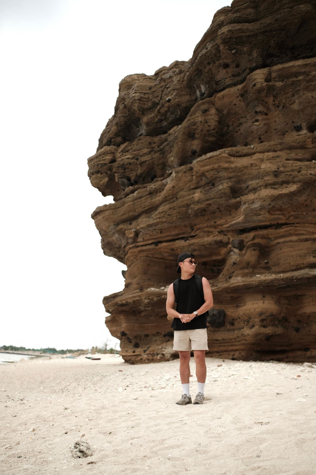 A man standing on the beach beneath a huge layered rock overhang