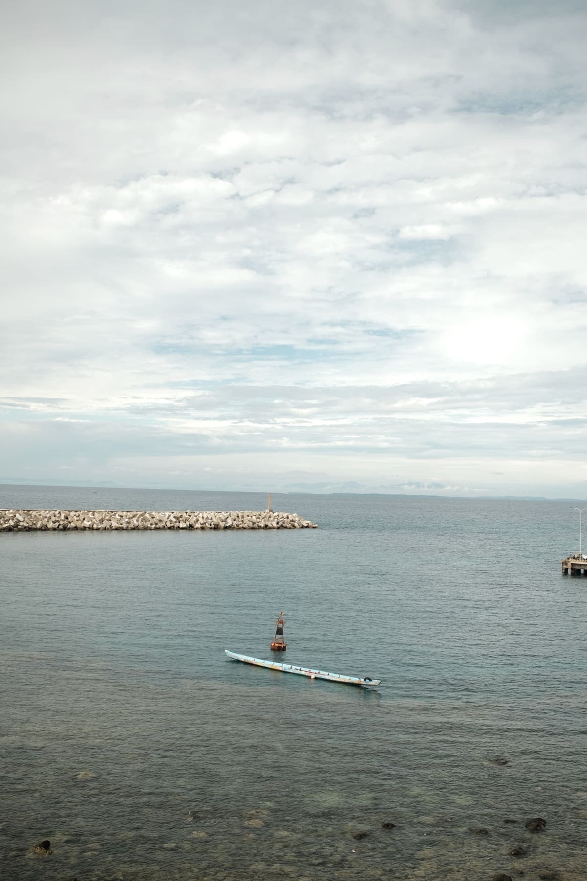 A small boat on calm water near a breakwater under a cloudy sky