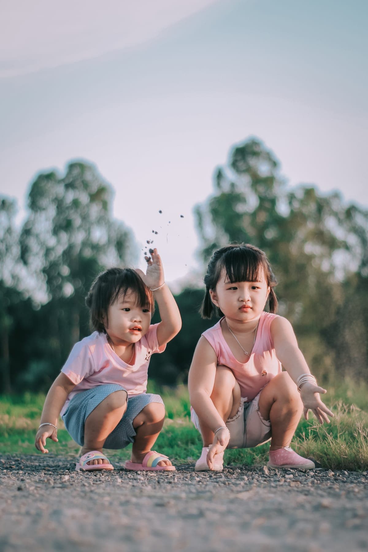 Two little girls crouching on the path, one tossing a handful of grass seeds