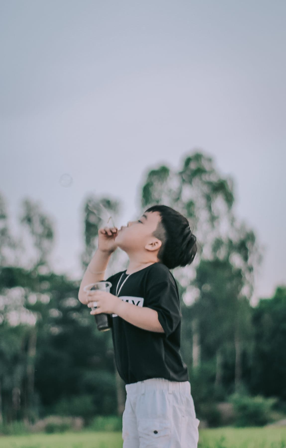 A boy blowing bubbles in front of a row of tall trees