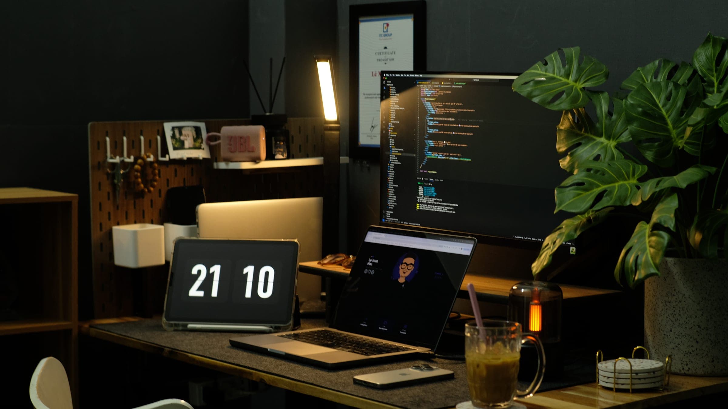 A desk at night with code on the monitor, a laptop and a flip clock showing 21:10